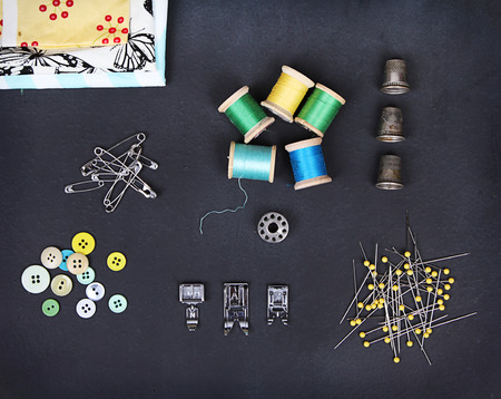 A collection of sewing items including: thread, thimbles, pins, buttons, bobbin, sewing machine feet and material on a chalkboard backgroundの写真素材
