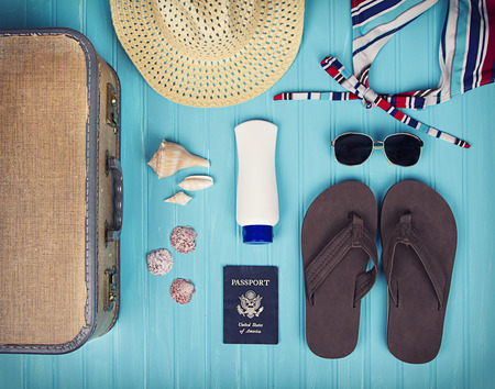 A collection of travel items including suitcase, passport, sandals, sunglasses, swim suit, sunscreen and straw hat on turquoise backgroundの写真素材