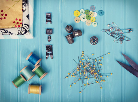 A collection of sewing items including: thread, thimbles, pins, buttons, bobbin, sewing machine feet and material on a turquoise backgroundの写真素材