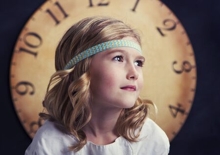 Young girl looking to the side with a large vintage clock behind herの写真素材