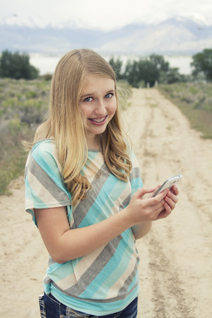Teenage girl using cellphone walking down a country dirt road outdoors in a rural areaの写真素材