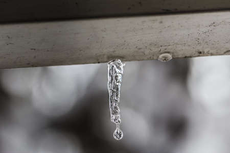 Water drop falling from icicle hanging from weathered awning after snowstorm の写真素材