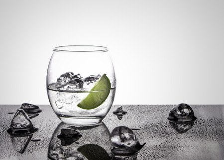 Vodka or Gin with lime in an oval glass on a glossy base with ice cubes against a white back lit backgroundの写真素材
