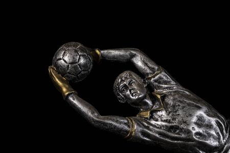 A silver trophy of a football (soccer) goalkeeper with gold accents on a black background for a presentation ceremonyの写真素材
