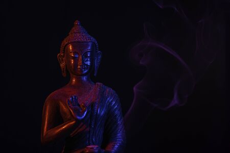 A religious ornamental buddha figure lit by red and blue flashes on a black background with copy spaceの写真素材
