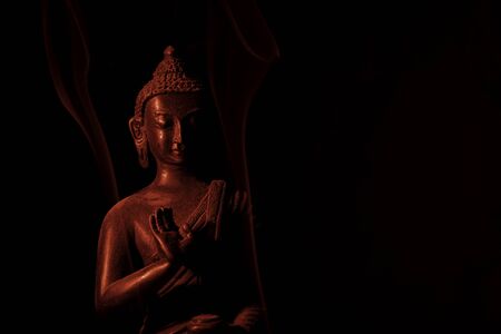 A religious ornamental buddha figure lit by a red flash on a black background with copy spaceの写真素材