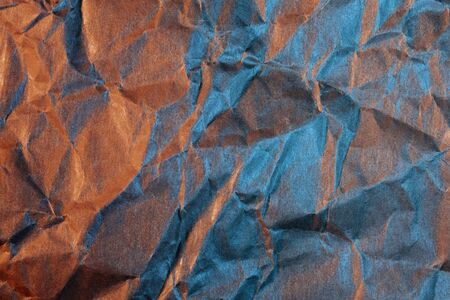 A close up abstract macro photo of crumpled creased paper lit with cyan and red flash gels
