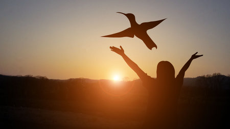 A man with a cross at sunset, a golden light beneath a flying bird, indicates the joy of freedom and...
