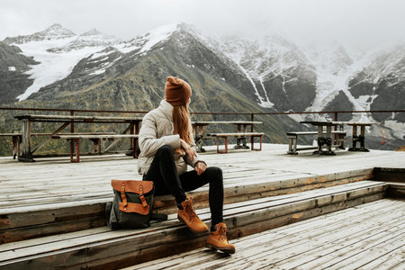 Girl traveler with backpack enjoy mountain nature sitting on wooden bridge. Cheget, Kabardino-Balkaria, Russia.の写真素材