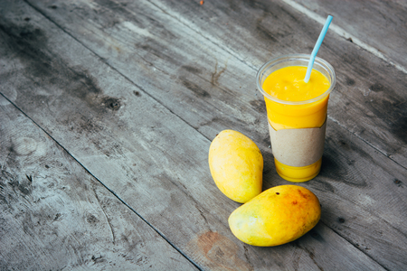 Mango smoothie in glass and mango fruits on wooden table Fruit shake background. Healthy drink...