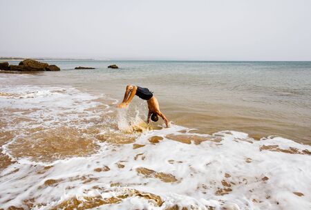 Young boy jumping over the waves breaking on the beachの写真素材
