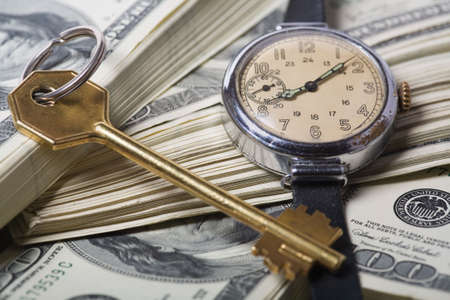 Conceptual keys to success of time and money. Rich colors and clear shot with skeleton key, US currency, a small modern watch that portrays spending, finance, business success. の写真素材