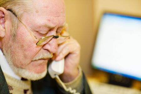 Mature businessman talking on the phone and checking out a document on his computer monitor. 