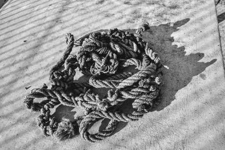 Rope and shadows during sunny day .. An old and frayed rope standing in a mess. Old rope standing on the concrete floor and its shadow is shown.の写真素材