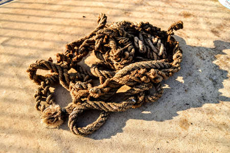 Rope and shadows during sunny day .. An old and frayed rope standing in a mess. Old rope standing on the concrete floor and its shadow is shown.の写真素材