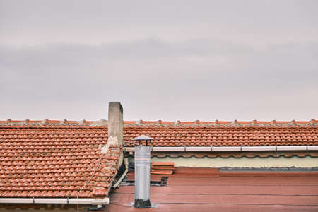 Red bricks roof, metal and concrete made of chimneys and overcast sky background.