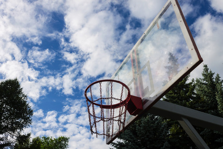 Basketball ring against the sky with clouds and trees