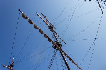 Mast of an old ship with raised sails against a clear blue sky