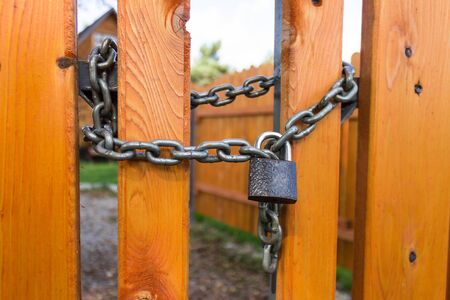 Padlock and steel thick chain on a bright yellow wooden fenceの写真素材