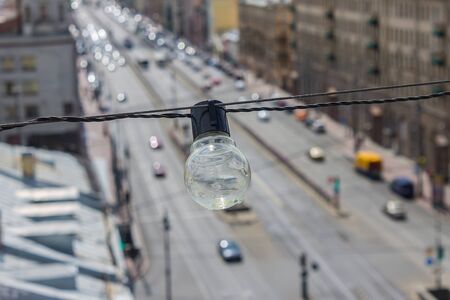 A wet electric lamp hangs over a busy city road and house roofsの写真素材