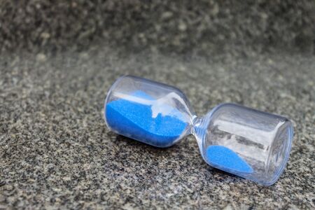 Glass hourglass with blue granules lie on gray granite