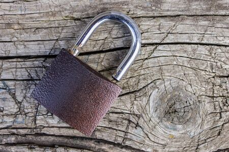 A padlock lies on an old, wooden board with cracks and scratchesの写真素材