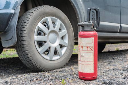 A fire extinguisher stands on the ground near the car as fire safety. Road fire prevention