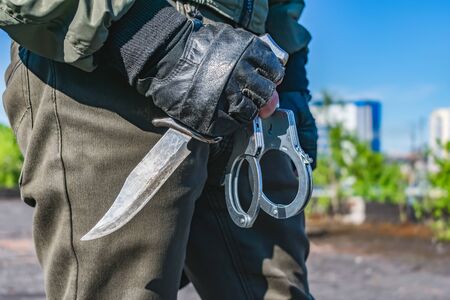 A commando holds handcuffs and a knife on the ready