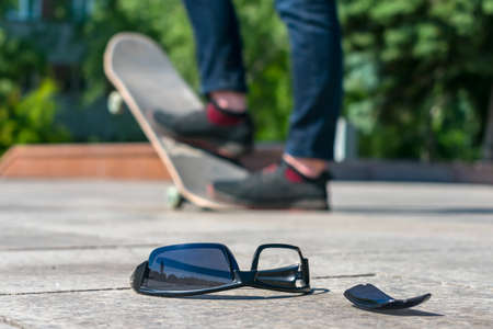 Lost black glasses lie on the road against the background of a man skating on a skateboardの写真素材