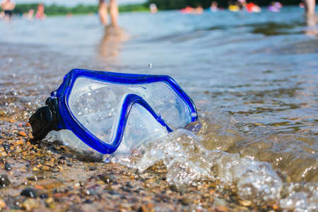 Scuba diving mask lost and thrown ashore with people resting in the backgroundの写真素材