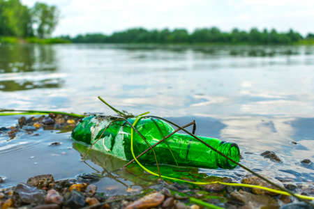 Glass bottle on the riverbank pollutes the environment. Nature pollution with garbage left by vacationers on the beachの写真素材
