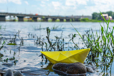 A paper boat shipwreck near a rocky river bank. Conceptual photo showing potential hazards in maritime transportの写真素材