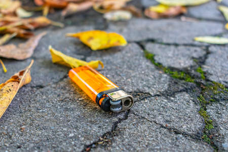 Lost orange pocket lighter lies on the road among fallen autumn leavesの写真素材