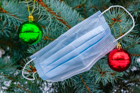Spruce branches with Christmas decorations and a medical mask as a symbol of new time and reality in a pandemicの写真素材