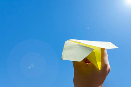 People have fun launching yellow paper airplane into clear blue skyの写真素材