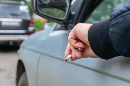 The driver stuck out his hand while holding a cigarette out of the window of his car, enjoying smoking and harming his healthの写真素材