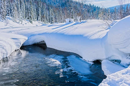The stream of mountain water breaks through the snowの写真素材