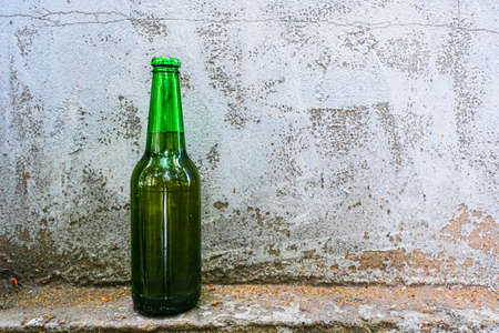 A bottle with an alcoholic drink stands against an old concrete wallの写真素材