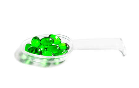 green capsules on a teaspoon isolated on white backgroundの写真素材