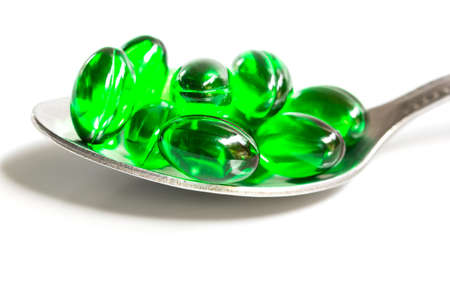 green capsules on a teaspoon isolated on white backgroundの写真素材