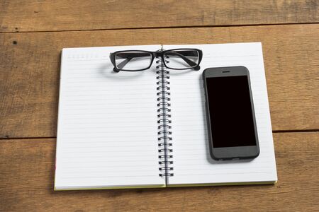 Notebook with glasses and smart phone on wooden background.の写真素材