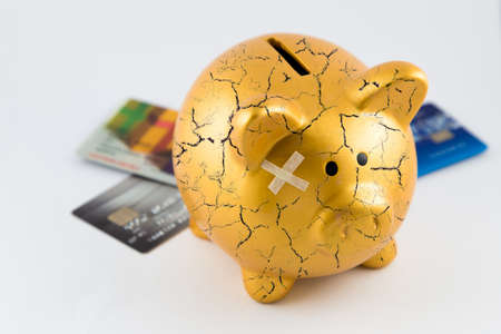 Right side of gold piggy bank cracked with plaster and blurred credit cards on isolated white...