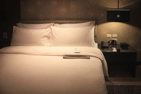 King size bed, blanket and pillow with white cotton cover which shining by lamp on the wall.の写真素材
