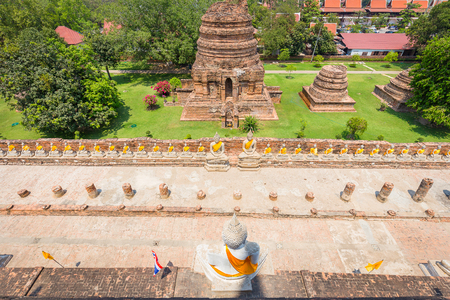 Top view on white buddha statue and small statue of monks in Wat Yai Chaimongkol of Ayutthaya, Thailand. With background of pagodas in the green field.の写真素材