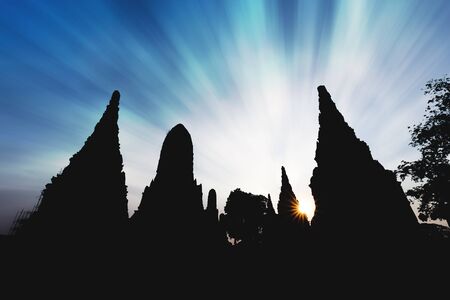 Silhouetted pagoda and temple with sunset and dramatic cloudy blue sky in Wat Chaiwatthanaram of Ayutthaya, Thailand.の写真素材