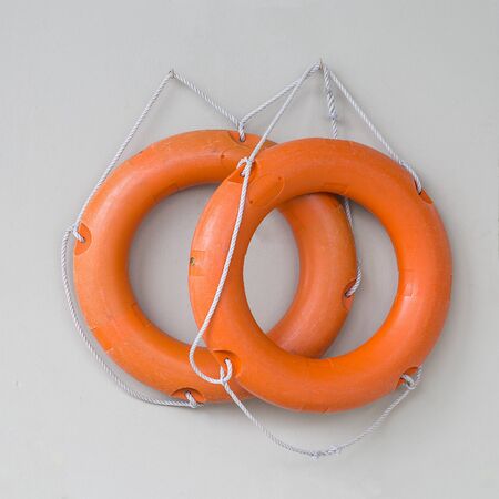 Two orange life rings with white rope hanging on gray wall near swimming pool