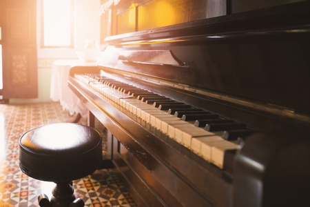Side view of old and cracked piano and stool with orange warm tone from sunlight through windowの写真素材