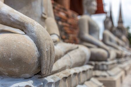 Close focus on hand of meditating monk statue in the row of many statues inside brick temple called Wat Yai Chai Mongkol in Ayutthaya of Thailandの写真素材