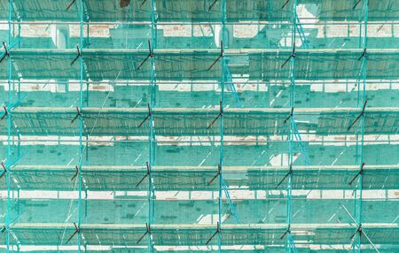 Scaffolding in difference levels with green transparency covering net attached old building on maintenance period.の写真素材