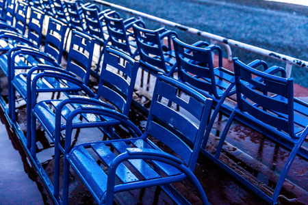 Morning scene of blue chairs array as straight line wet water after raining on street for serving...